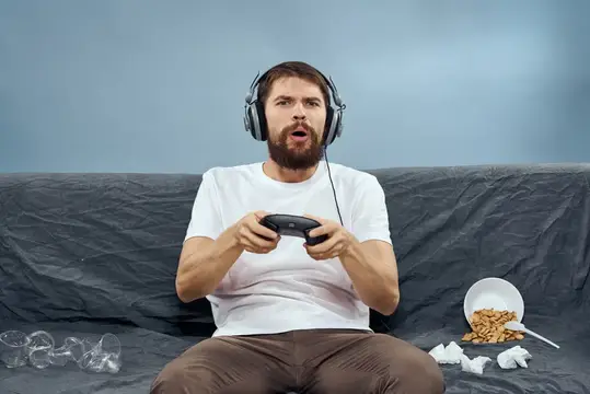 Веселый мужчина сидит на диване и играет с развлекательной техникой