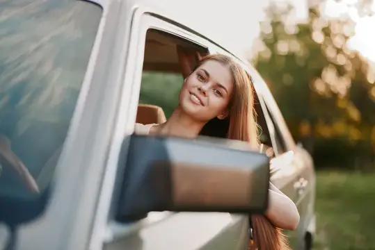 Улыбающаяся девушка с длинными волосами выглядывает из окна автомобиля