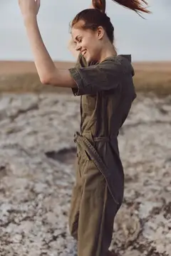 Женщина в оливковом комбинезоне стоит на каменистом поле, подняв руки вверх, для обложки журнала мод и красоты