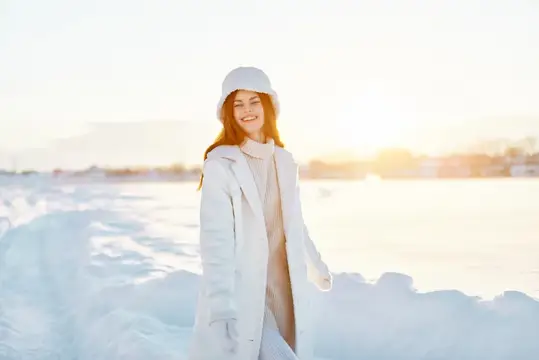 Улыбающаяся девушка в белом пальто и шапке на заснеженном берегу
