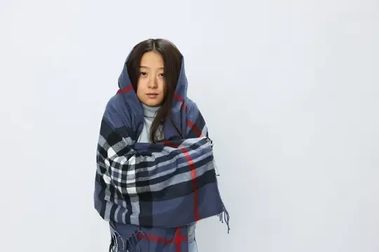 Азиатская девушка кутается в клетчатый плед на белом фоне