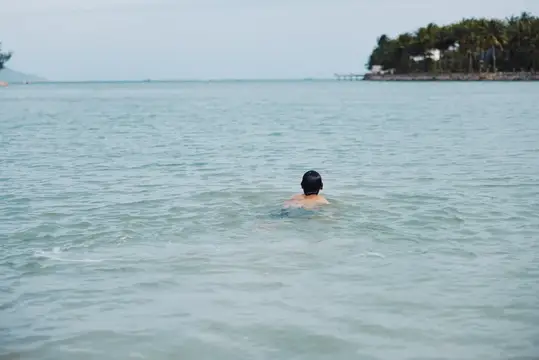 Мужчина в тёмной шапочке плывёт в спокойном море у тропического берега