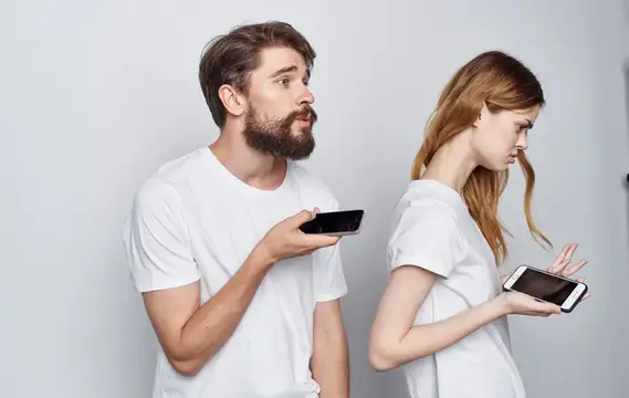 Бородатый мужчина и рыжеволосая женщина со смартфонами у стены