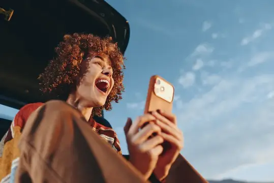 Женщина смеется и держит смартфон для селфи