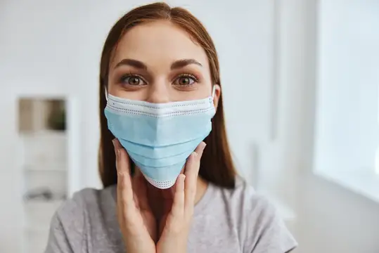 Молодая женщина в медицинской маске держится за лицо руками