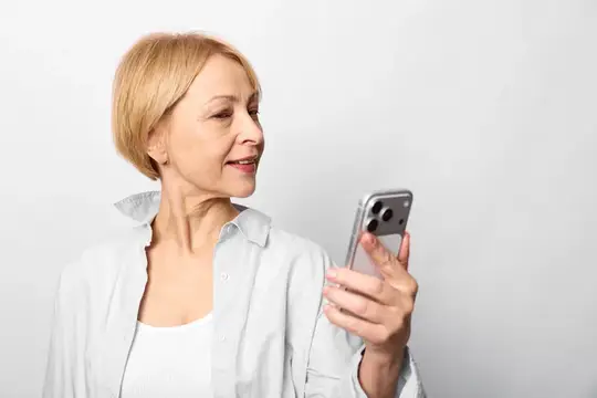 Улыбающаяся блондинка держит смартфон на светлом фоне
