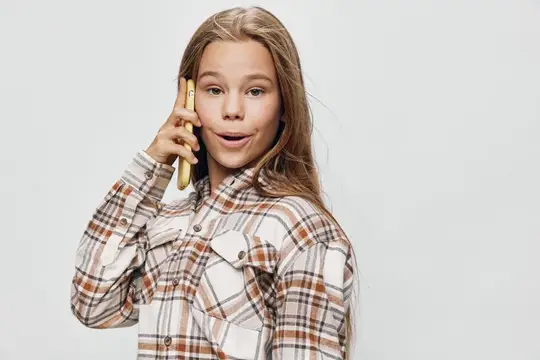 Светловолосая девочка в клетчатой рубашке говорит по телефону