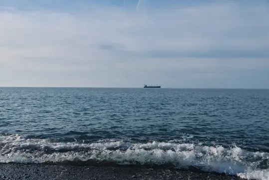 Одинокий грузовой корабль на горизонте спокойного моря