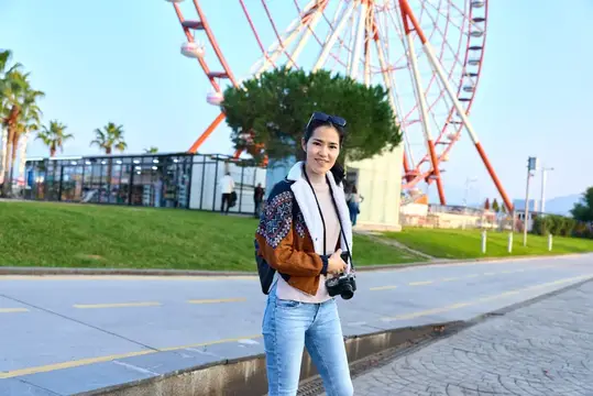 Улыбающаяся азиатская девушка с фотокамерой на фоне колеса обозрения