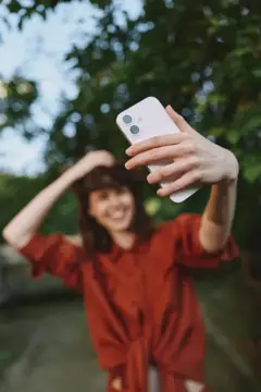 Улыбающаяся девушка в красной рубашке делает селфи на смартфон