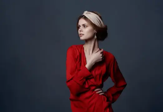 Молодая женщина в красном платье и светлой повязке на тёмном фоне
