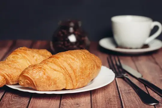 Свежие круассаны на тарелке рядом с чашкой кофе