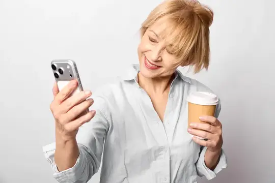 Улыбающаяся блондинка со смартфоном и кофе в руках