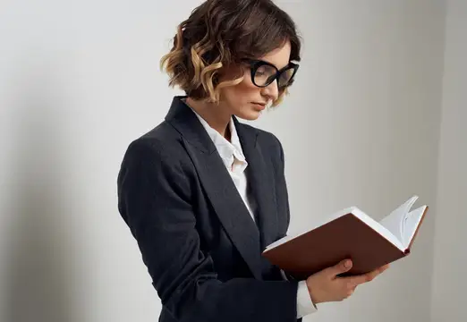 Молодая женщина в очках и деловом костюме читает книгу