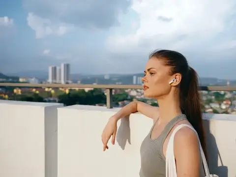 Молодая женщина в наушниках смотрит на город с крыши