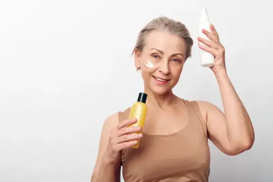 Улыбающаяся седовласая женщина с косметикой и кремом на щеке
