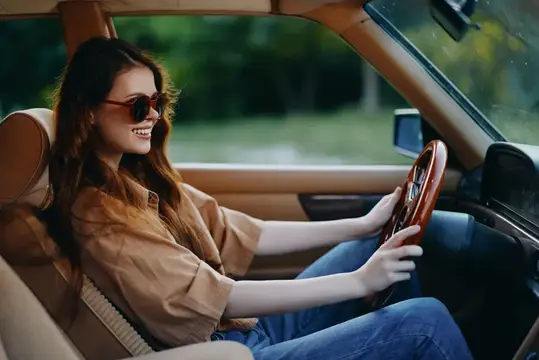 Улыбающаяся темноволосая девушка в солнцезащитных очках за рулём автомобиля