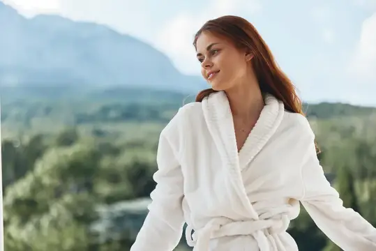 Молодая женщина в белом халате улыбается на фоне гор и зелени