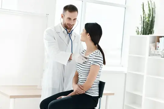 Врач с стетоскопом осматривает улыбающуюся пациентку в светлом кабинете