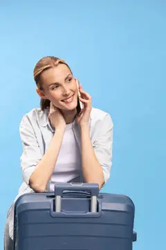 Улыбающаяся светловолосая девушка с чемоданом говорит по телефону