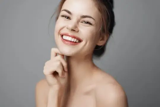 Улыбающаяся молодая женщина с ямочками на щеках на сером фоне