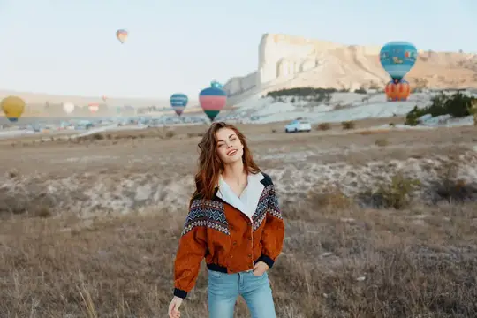 Молодая женщина в узорчатой куртке позирует на фоне воздушных шаров в Каппадокии