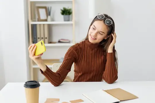 Улыбающаяся девушка с жёлтым смартфоном за рабочим столом