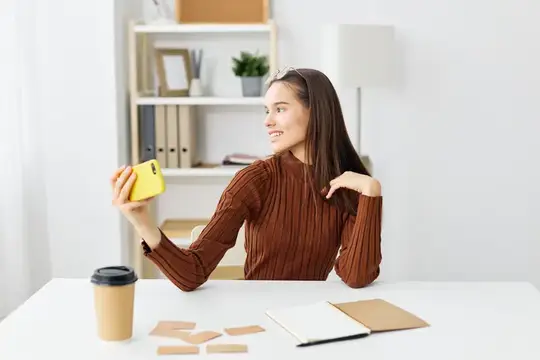 Улыбающаяся девушка с жёлтым смартфоном за рабочим столом