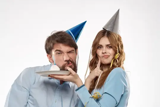 Мужчина и женщина в праздничных колпаках дурачатся с тортом