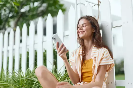 Улыбающаяся девушка с телефоном у белого забора
