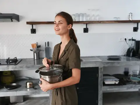 Улыбающаяся женщина держит кастрюлю на светлой кухне