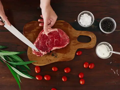 Руки нарезают сырой стейк на деревянной доске