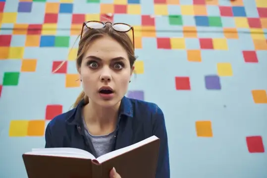 Удивлённая девушка с книгой на фоне цветной стены