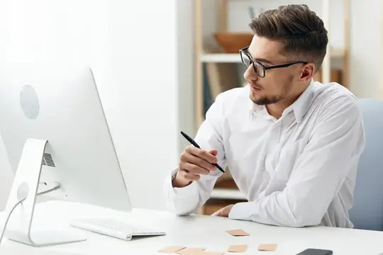 Молодой мужчина в очках работает за компьютером в светлом офисе