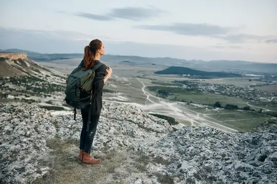 Девушка с рюкзаком любуется долиной с каменистой вершины