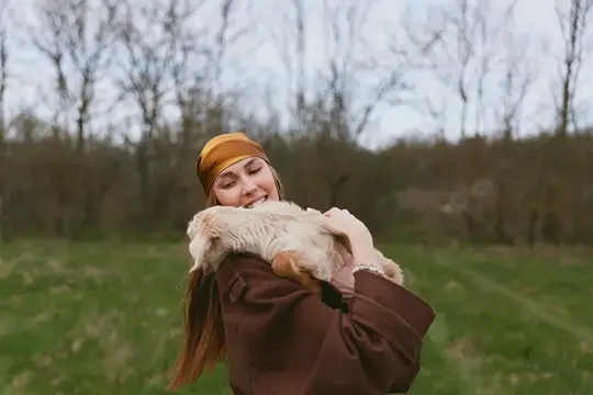 Ласковая сцена женщины и козлёнка на улице, повседневная одежда, деревенская обстановка, мягкий свет, непринуждённое настроение, повседневное счастье и связь с природой