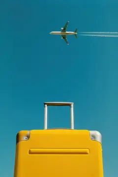 Желтый чемодан и самолет, летящие в голубом небе
