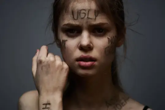 Молодая девушка с надписью UGLY на лбу и испуганным взглядом