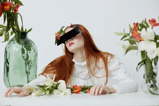 Модная молодая женщина в белом платье и черных солнцезащитных очках с рыжими волосами позирует среди ярких цветов, создавая безмятежную и элегантную атмосферу, что идеально подходит для тем красоты…
