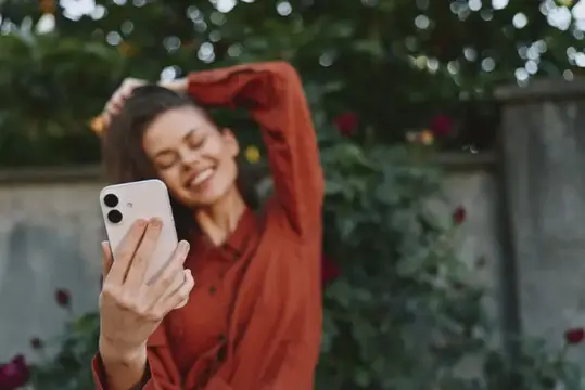 Улыбающаяся брюнетка в красной рубашке делает селфи на смартфон