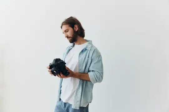 Бородатый мужчина в голубой рубашке рассматривает фотокамеру