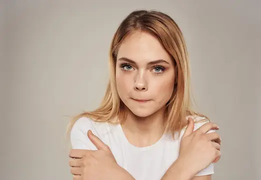 Светловолосая девушка обнимает себя за плечи на сером фоне