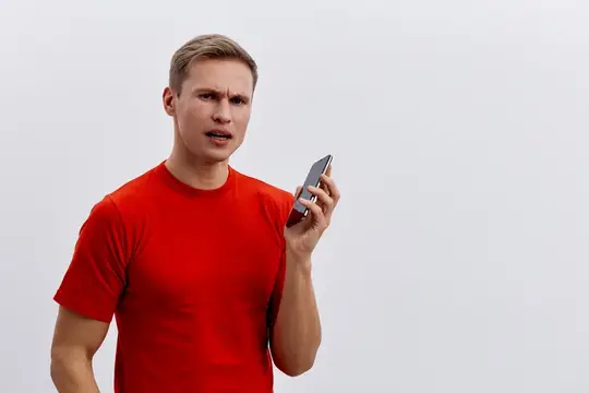 Светловолосый мужчина в красной футболке удивлённо смотрит на телефон