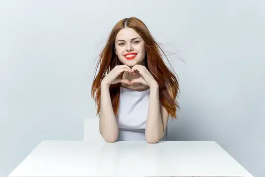 Симпатичная женщина сидит за столом и жестикулирует руками, её красные губы подчёркивают стиль жизни