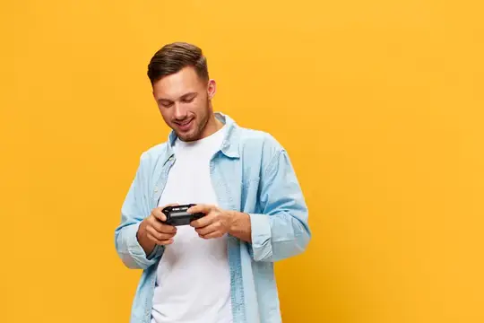Молодой мужчина с улыбкой играет в игры на смартфоне на жёлтом фоне