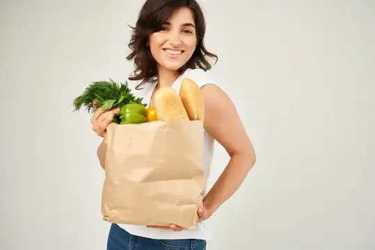 Улыбающаяся брюнетка держит бумажный пакет с продуктами