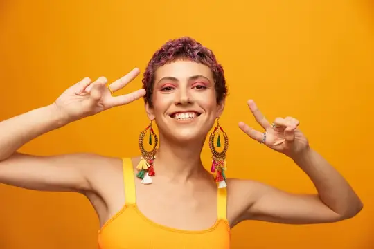 Улыбчивая девушка с фиолетовыми кудрями показывает два жеста мира на оранжевом фоне