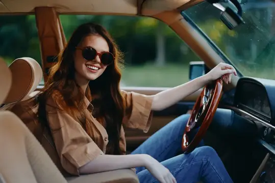 Улыбающаяся девушка в солнцезащитных очках за рулём автомобиля