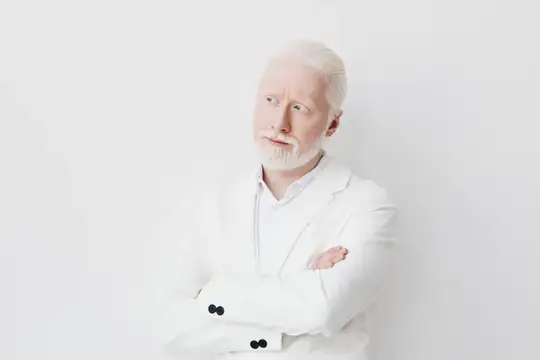 Альбинос в белом костюме со скрещёнными руками на светлом фоне