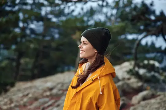 Улыбающаяся девушка в жёлтой куртке и шапке на фоне леса